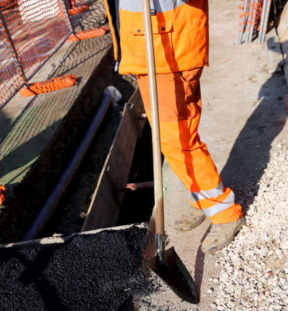 workers in a road construction site with high visibility pants and a working shovel in handの写真素材