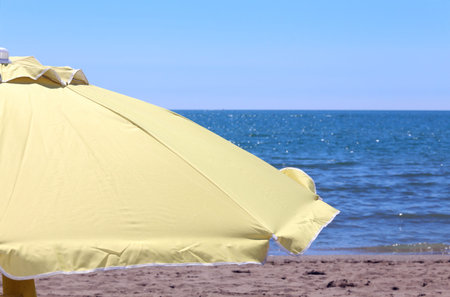 Large yellow sun umbrella on the shore of the ocean in the hot sunny dayの写真素材