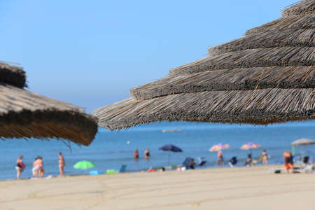 Large straw beach umbrella to shelter from the hot summer sun by the sea with many people in the oceanのeditorial素材