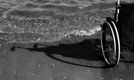 Shadow of wheelchair on the sand of the beach by the ocean in black and white effectの写真素材