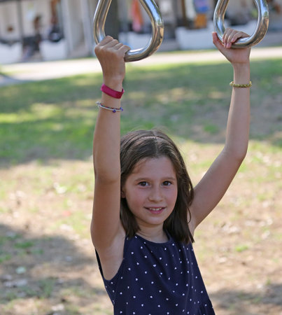 Caucasian little girl dressed in blue while performing exercise exercises at the rings
