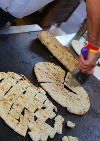 cook's hand while cutting the cooked flat bread also called piadina in italian language on the hot plate in the street food stand kioskの写真素材