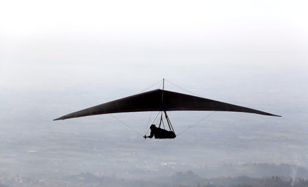 silhouette of a man flying high with his hang glider above the plainの写真素材