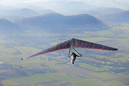 extreme sport with a man flying high with his hang glider above the plain