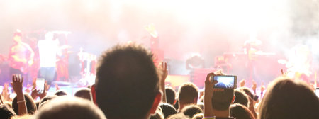 fans take photos and record videos with modern smartphones during live concert of a rock band on...