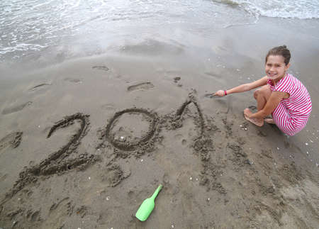 pretty little girl near the sea writes the text of the year 2017 on the sandの写真素材