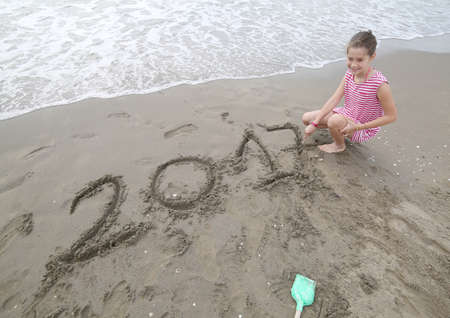 happy little girl near the sea writes the text of the year 2017 on the sandの写真素材