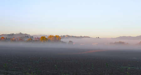 foggy autumn day with cultivated field and hills in the backgroundの写真素材