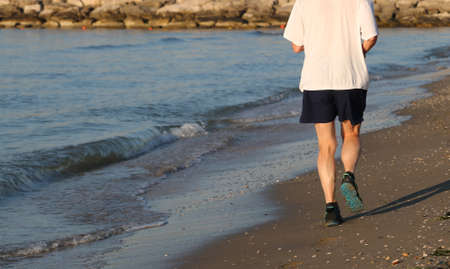 elderly person jogging on the beach by the sea at dawnの写真素材