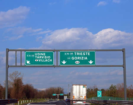 Italian highway with the road sign with directions to Udine Tarvisio and Austria or to Trieste at the crossroads of the roadの写真素材