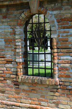 Window with metal grating and brick wall of the ancient convent
