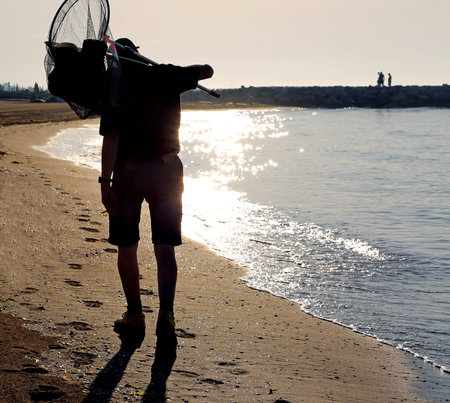 tired fisherman with nets walks on the shore of the sea at dawnの写真素材
