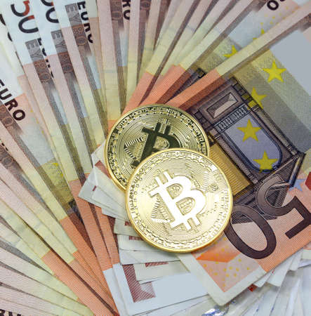 two big golden BitCoin coins over a lot of euro banknotesの写真素材