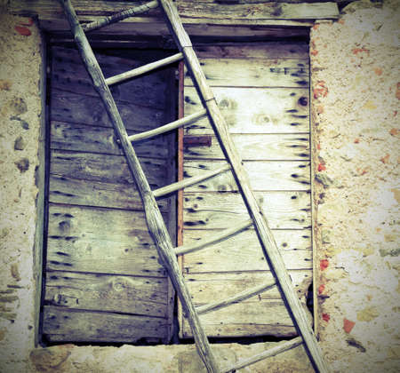 rural Scene with ancient ladder and a wooden old door of a farm with vintage effectの写真素材