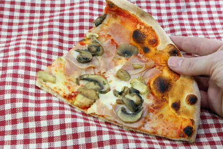 hand grabbing a slice of italian pizza with mozzarella cheese mushrooms ham and tomato sauce at italian pizzeriaの写真素材