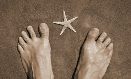 barefoot on the sand and starfish in summer with sepia toned effect
