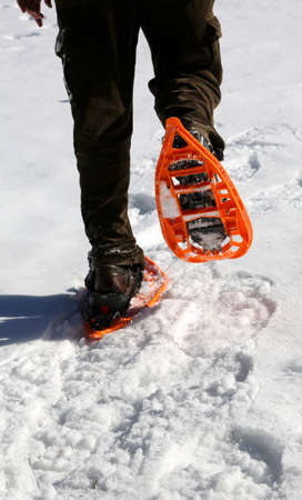 Man walks with modern orange snowshoes and corduroy pants on white fresh snow in winterの写真素材