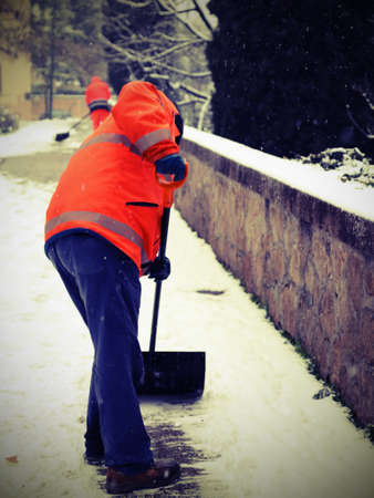 digger snow with high visibility vest shoveling the sidewalks after the snowfall with vintage effectの写真素材