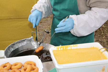 cook with blue gloves during the preparation of fried pancakes in the boiling oil
