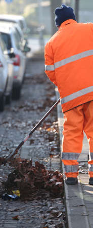 a street cleaner dressed in orange collects the dry leaves from the streetの写真素材