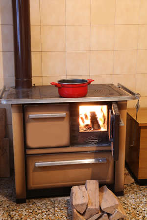 red pot over the old wood-burning stove in the kitchen of a mountain hut and fireの写真素材