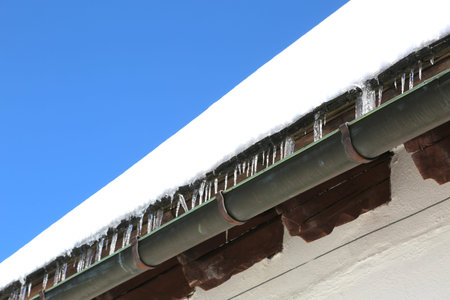 Gutter with icicles of ice on the roof after copious winter snowfall