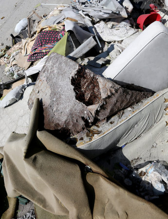 Broken old mattresses and dirty rags and garments in the abandoned homeless shelter after the forced...