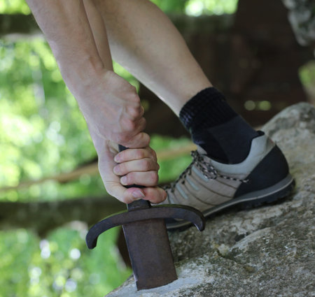 Excalibur Sword in the stone with the hand and a shoe of man that tries to remove from the rock