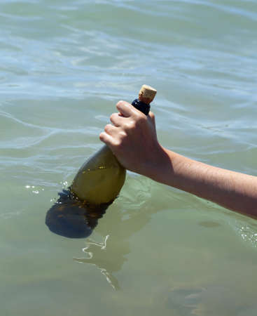 hand collecting the bottle with the secret message from the water of the seaの写真素材