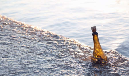 glass bottle with a secret message or a map by the sea at sunsetの写真素材