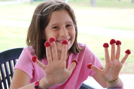 beautiful little girl with red raspberries on fingers hands