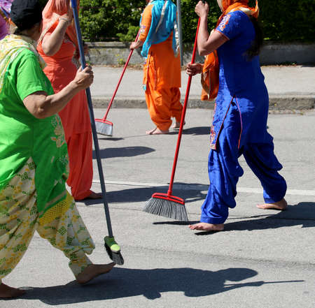barefoot Sikh women dressed in traditional clothes clean the street with brooms during a religious eventの写真素材