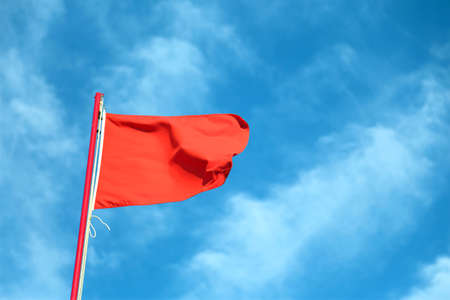 big red flag waving in the wind with the background of the blue sky and some cloudsの写真素材