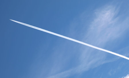 Engine exhaust contrails forming behind an airliner flying high in the blue sky