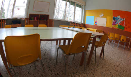 Inside a wide classroom of a Kingergarten with yellow chairs and small tables