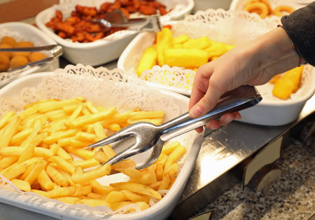 hand picking up many hot yellow french fries in the self-service restaurant