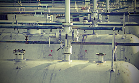 Many tanks in the storage of flammable materials of the industrial plant with valves and old toned...