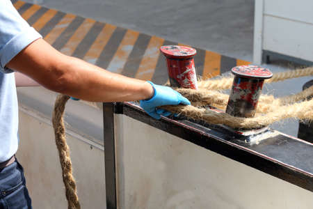 sailor ties a hemp rope to the dock to facilitate the mooring of a boatの写真素材