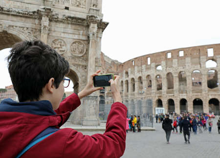 Young boy with glasses takes picture of Colosseum with his smart phone in Rome Italyの写真素材