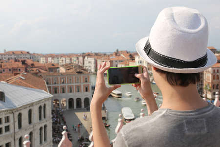 young boy with hat takes picutres with smartphone  in Venice Italyの写真素材