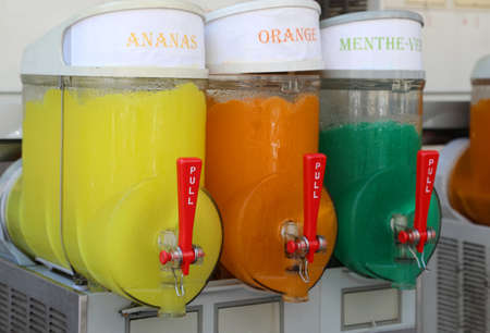 dispenser with many ice with syrup with text in french that means pineapple, orange and mintの写真素材