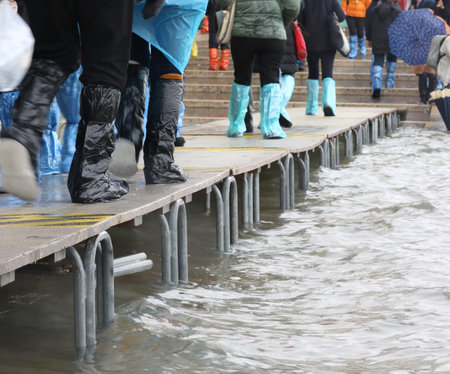 pedestrian boardwalk with people with plastic gaiters in Venice Italy during the flood