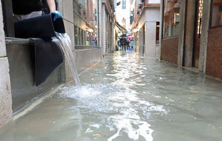Street of Venice called CALLE in Italian language with high water and a bucket to empty the storeの写真素材