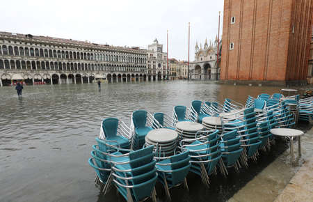 chairs of a sidewalk cafe in Saint Mark Square in Venice Itay with high tide and the bell tower in backgroundの写真素材