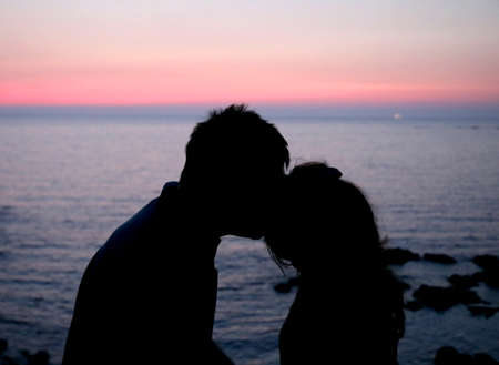 happy lovers lovingly kissing each other during a romantic sunset by the clear seaの写真素材