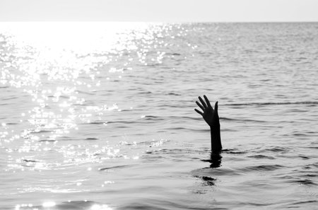 hand of a solitary man drowning in the ocean with black and white effect and backlight