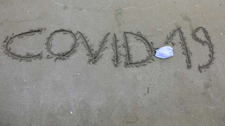 Text Covid-19 on the sand of the beach during the lockdown and the surgical maskの写真素材