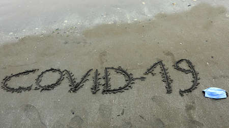 Text Covid-19 on the sand of the beach during the lockdown and the surgical maskの写真素材