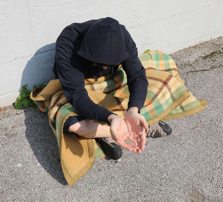 young homeless man begging on the street sitting cross-legged under an old blanketの写真素材