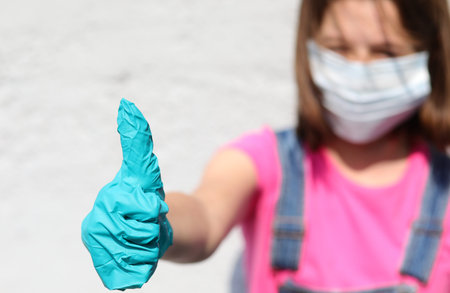 girl with mask and thumb up with latex glove for protection against Covid-19